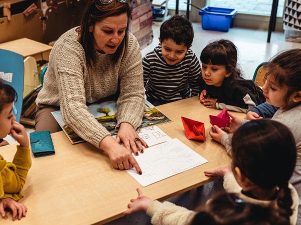 leerkracht wijst woorden op een blad aan, rondom haar zitten leerlingen samen aan tafel